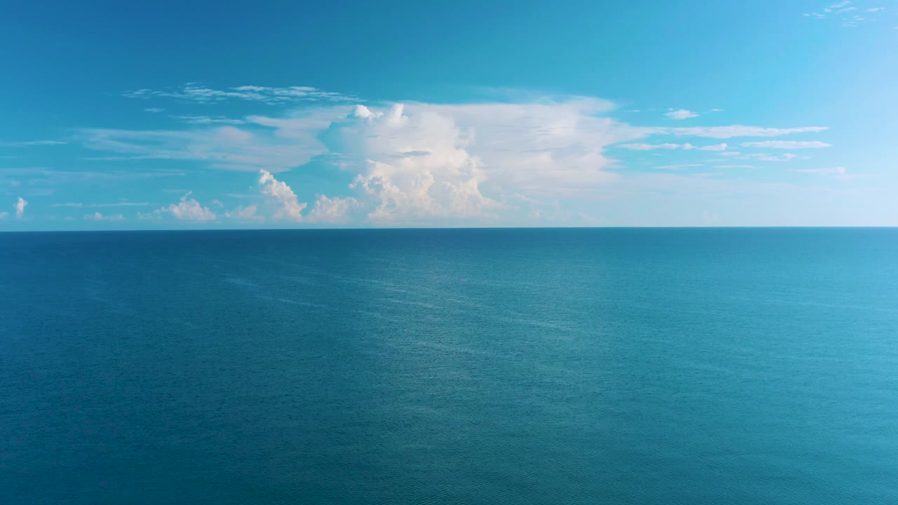 Mid-clip aerial view over La Ribera waters, with the ocean surface filling most of the frame, a large white cloud formation, and no visible people.