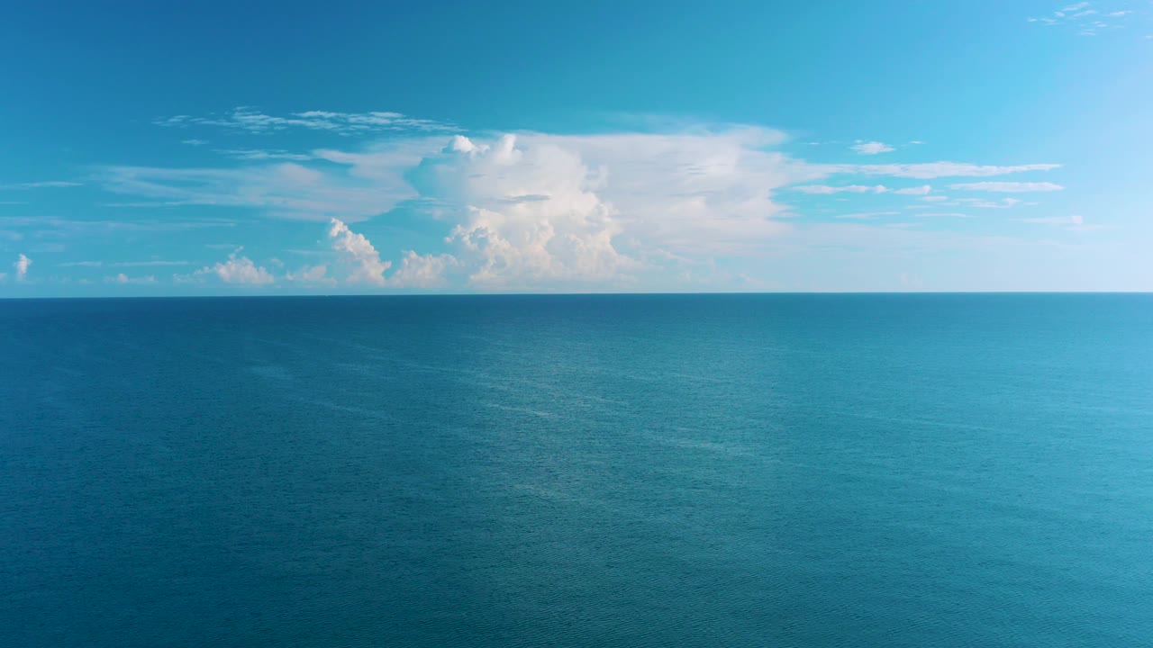 Wide blue ocean under bright sky and white clouds
