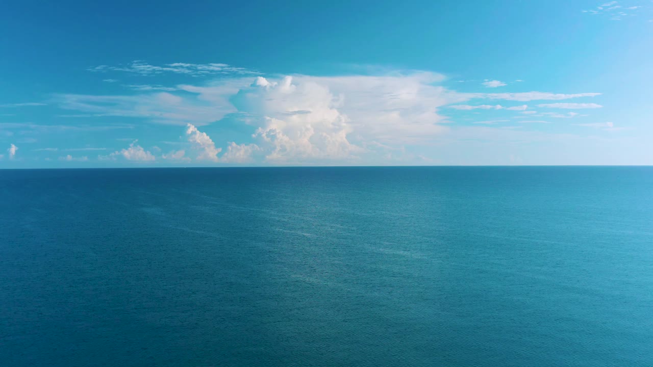 Blue water stretches to a flat horizon in La Ribera, Baja California Sur, with a large white cloud bank above the left side and no visible people.