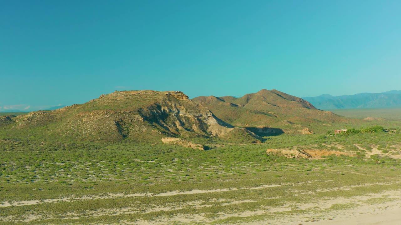 Scrub-covered terrain and rocky hills with a broad clear sky above.