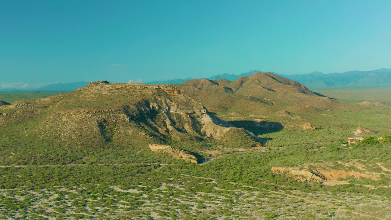 Drone view across rocky green hills with mountains on the horizon.