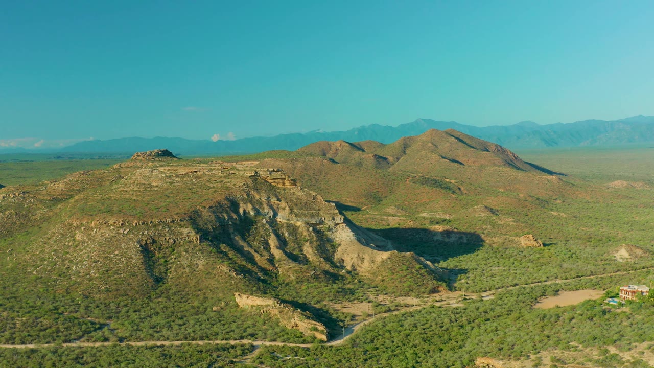 Aerial view of rocky hill shadow, green land, and distant ridges.
