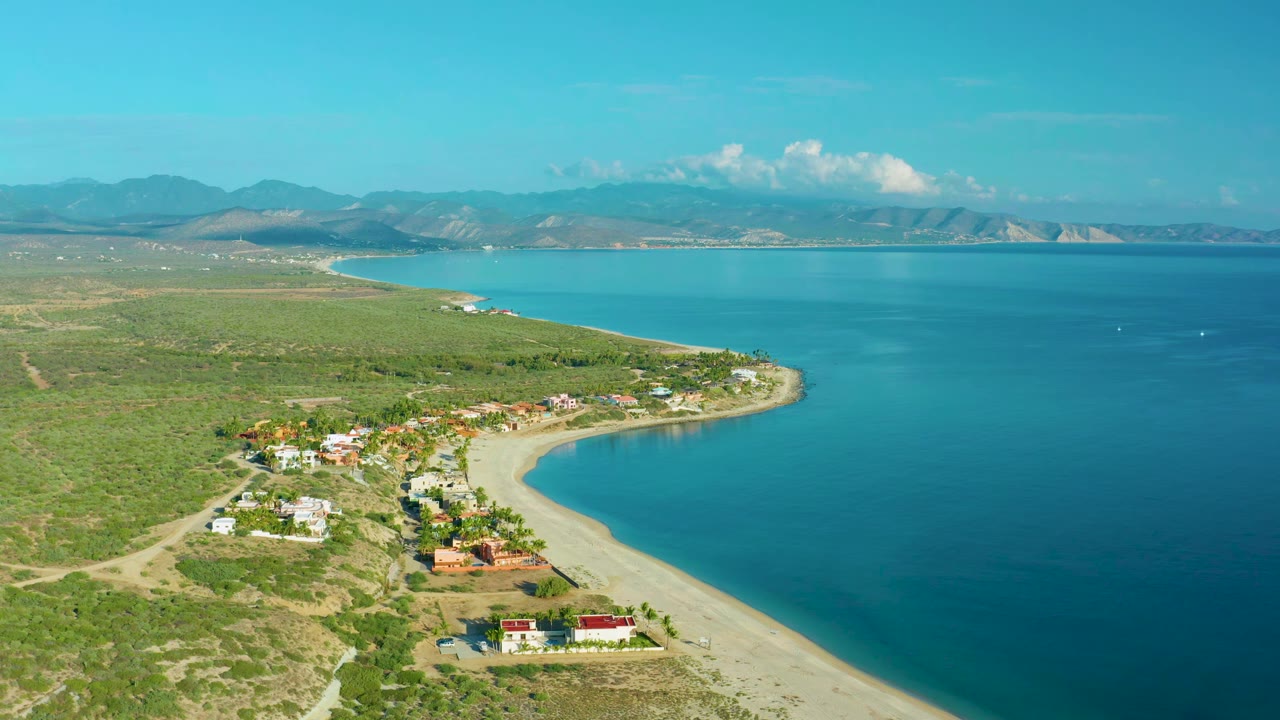 Wide aerial coastline with bay water, beach homes, scrubland, and mountains.