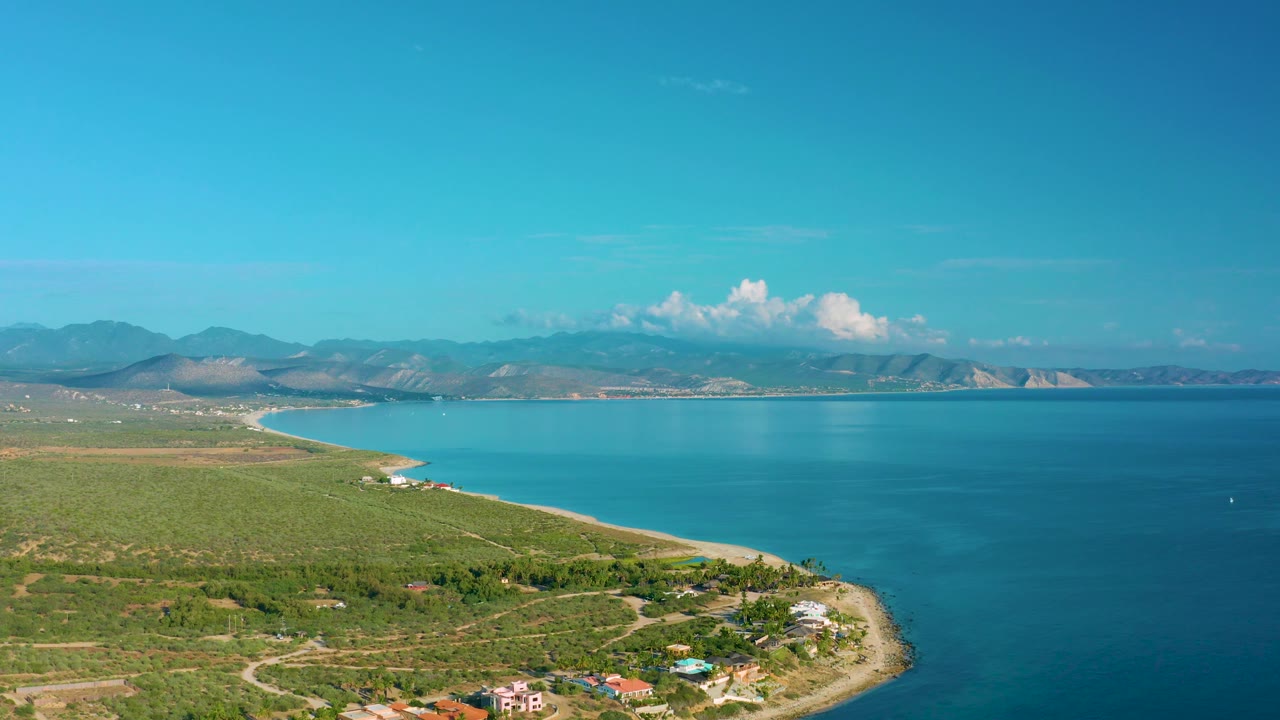 Elevated view across green coast, bright water, beach, and hazy mountains.