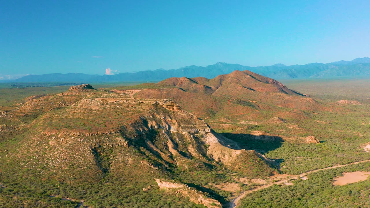 Opening aerial frame over rocky ridges and green desert scrub in La Ribera, Baja California Sur, with distant mountains and no visible people.