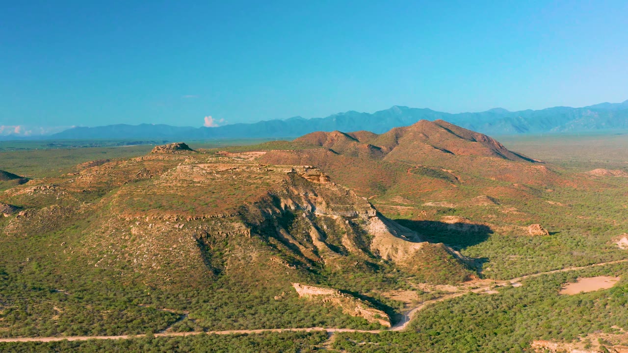 At 0:02, the aerial view shows the shadowed face of a scrubby ridge, pale exposed slopes, distant mountain silhouettes, and no visible people in La Ribera.