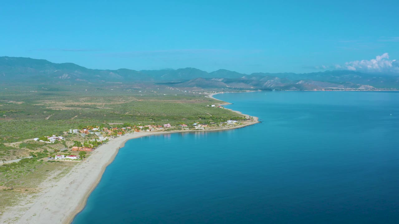 High coastal view with beach curve, village buildings, inland fields, and blue inlet.