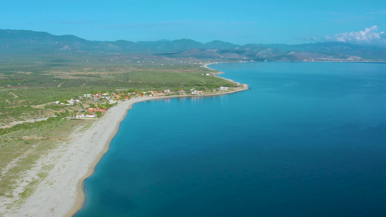 Aerial beach scene with turquoise shallows and inland mountain horizon.