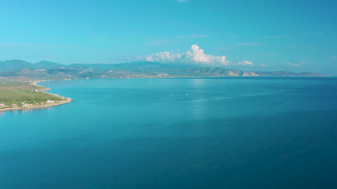 Wide sea aerial with curved coast at left and mountain range on the horizon.