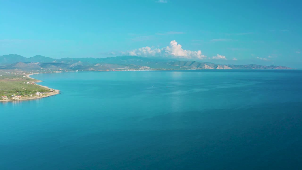 Blue coastal water with a curved shoreline and mountains under white clouds.