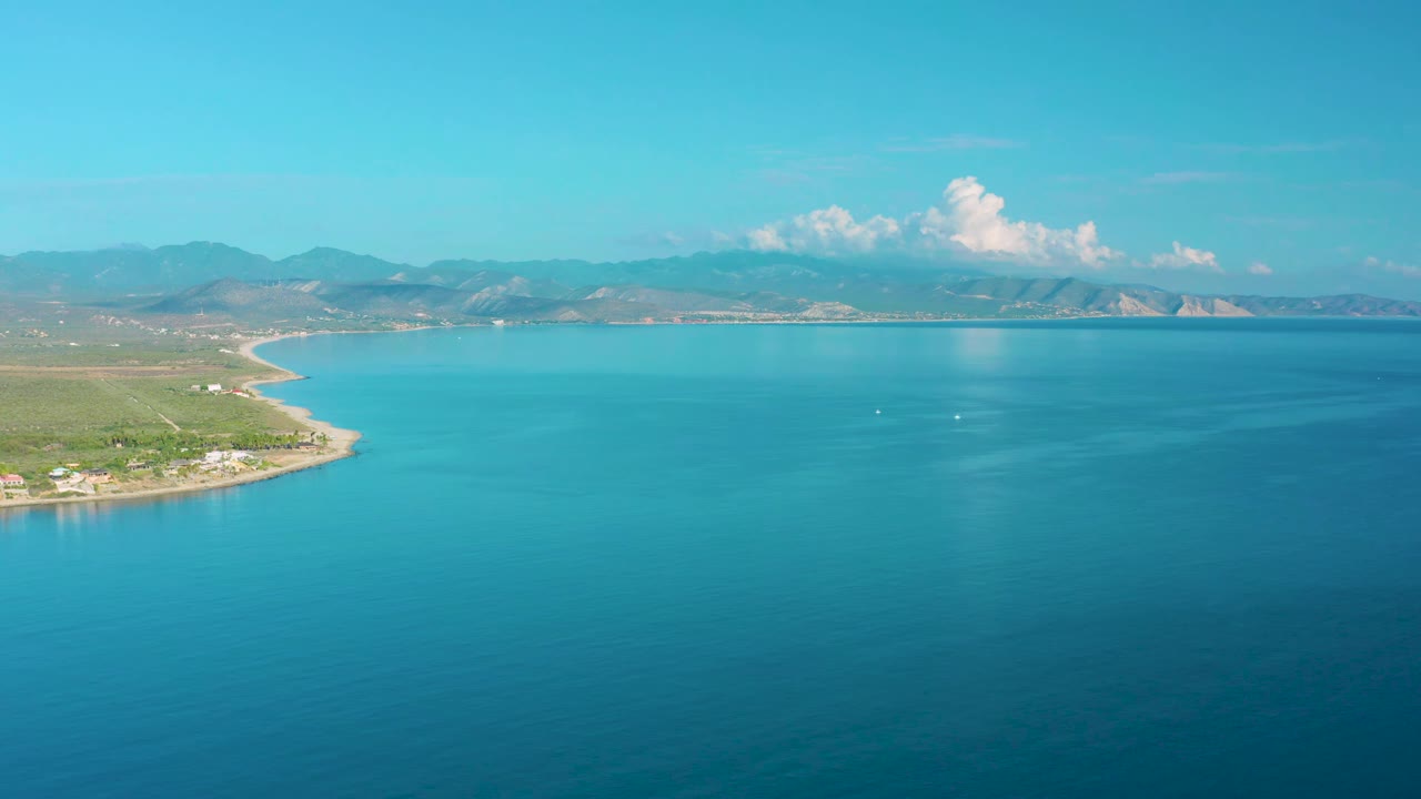 Aerial coastal water view with shoreline at left and mountains across the horizon.