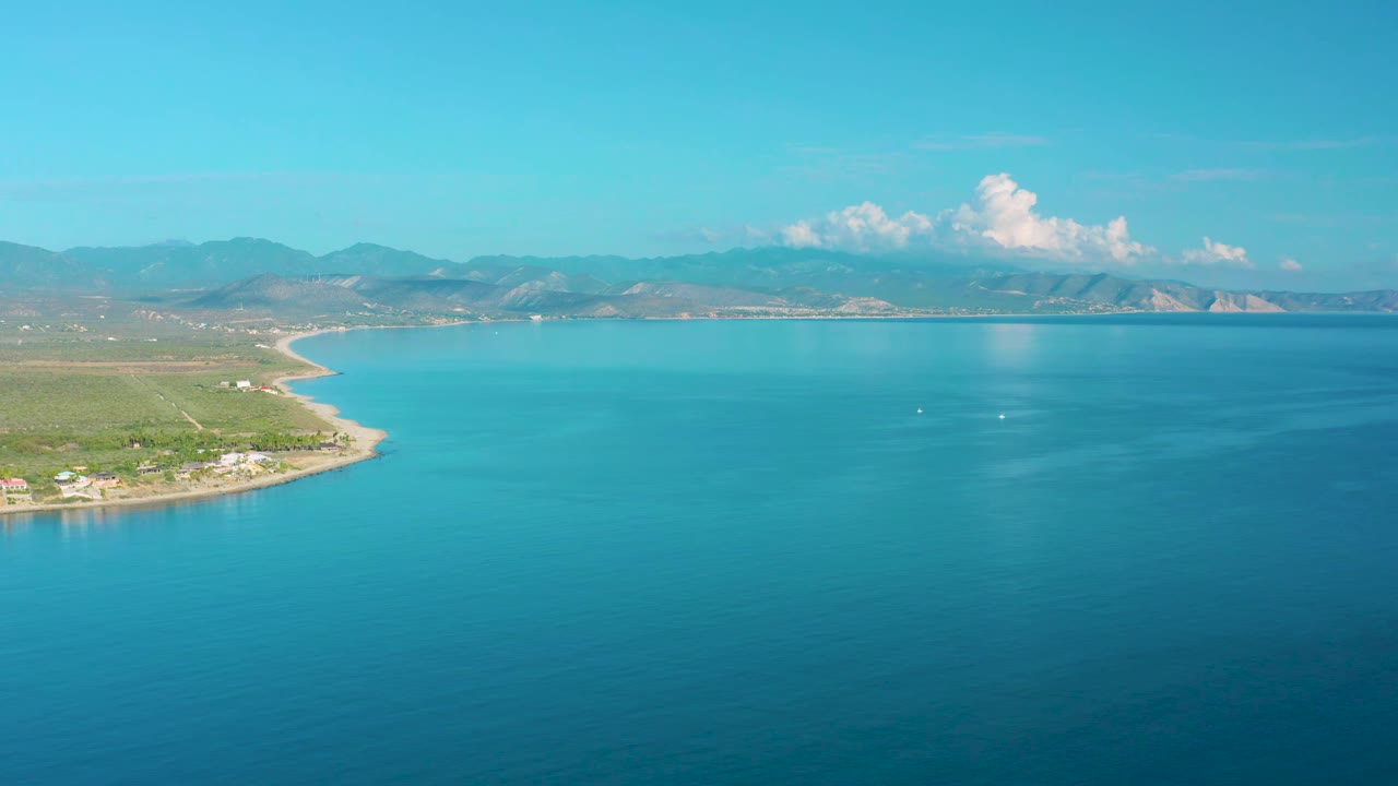Aerial coastline view with open blue water, shoreline at left, mountains, and clouds.