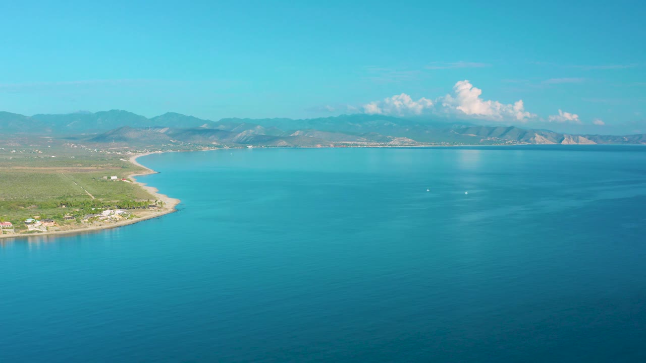 Third frame of the La Ribera aerial view holds a high horizon with the coastline on the left, calm turquoise water across the center, small buildings near shore, and no visible people.