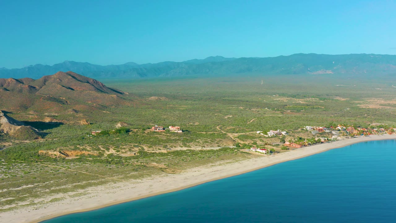 Aerial beach edge with hills and inland scrubland