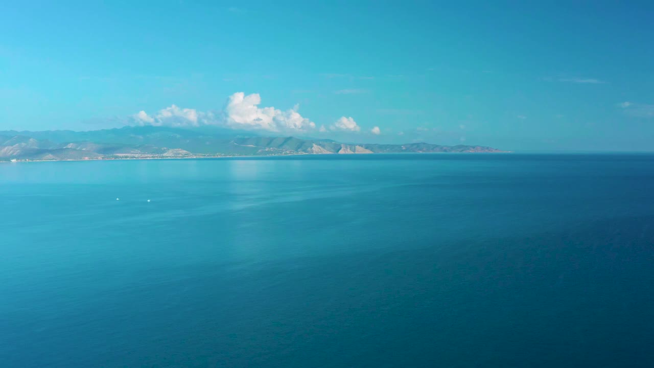 Wide blue ocean with distant mountains and white clouds on the horizon