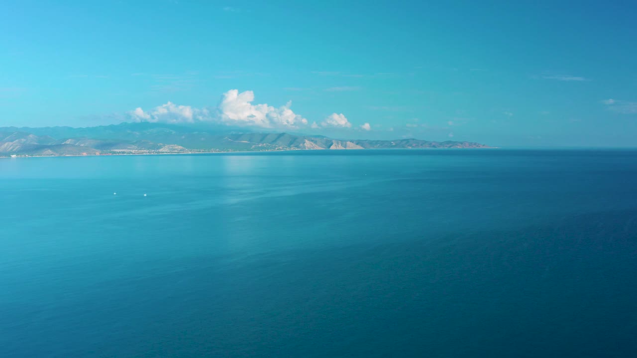 At 0:02, turquoise water shifts into deeper blue toward the foreground, with the La Ribera mountain horizon and cloud cluster still visible, and no visible people.