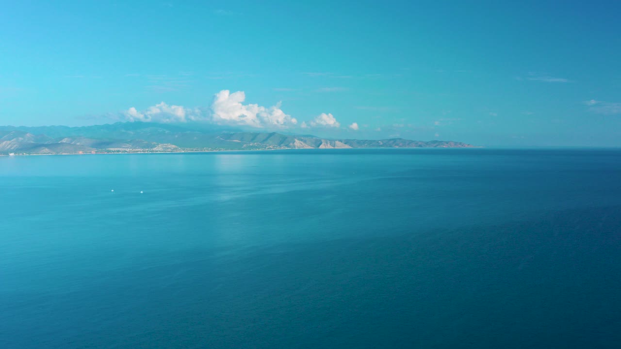 Blue ocean with distant mountains and white clouds
