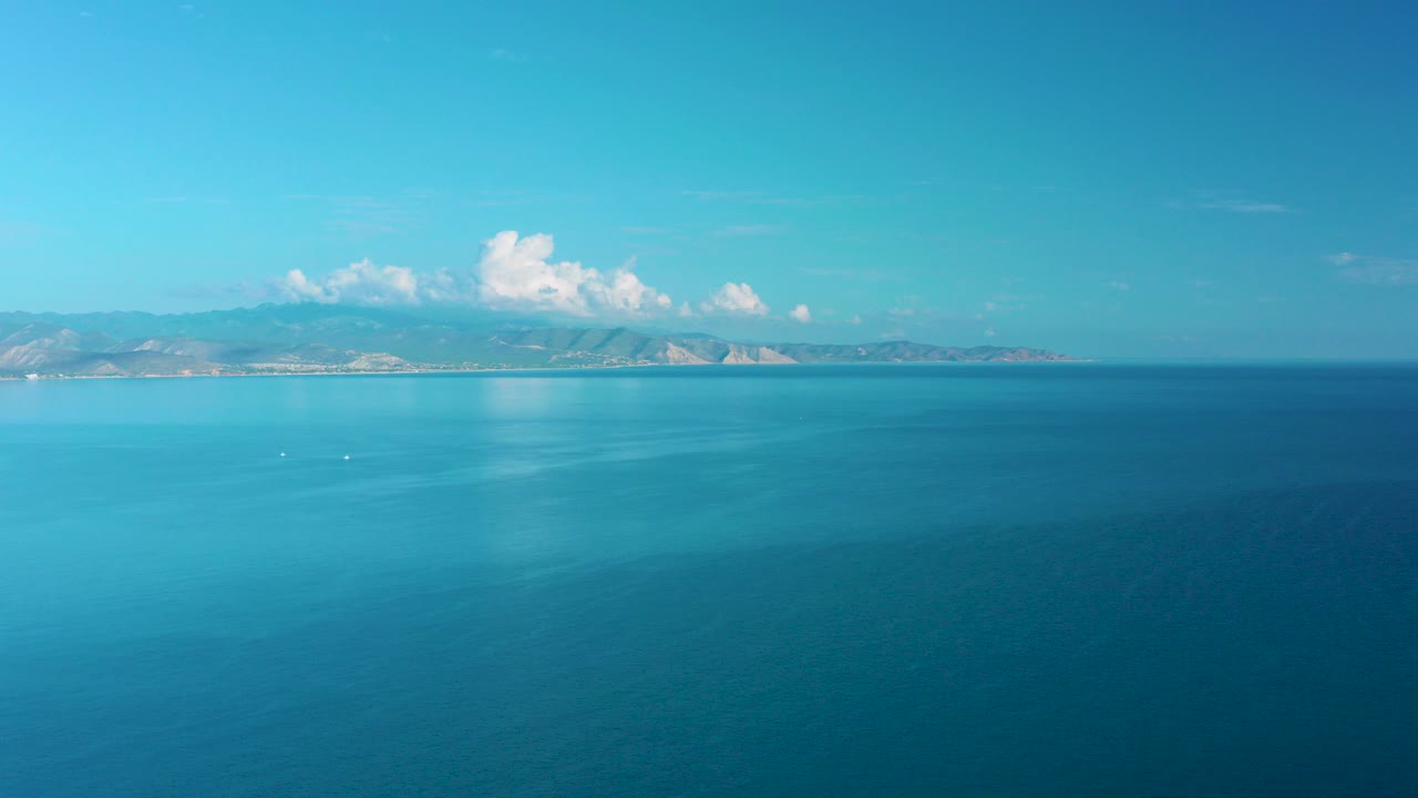 Turquoise ocean with distant mountains and white clouds