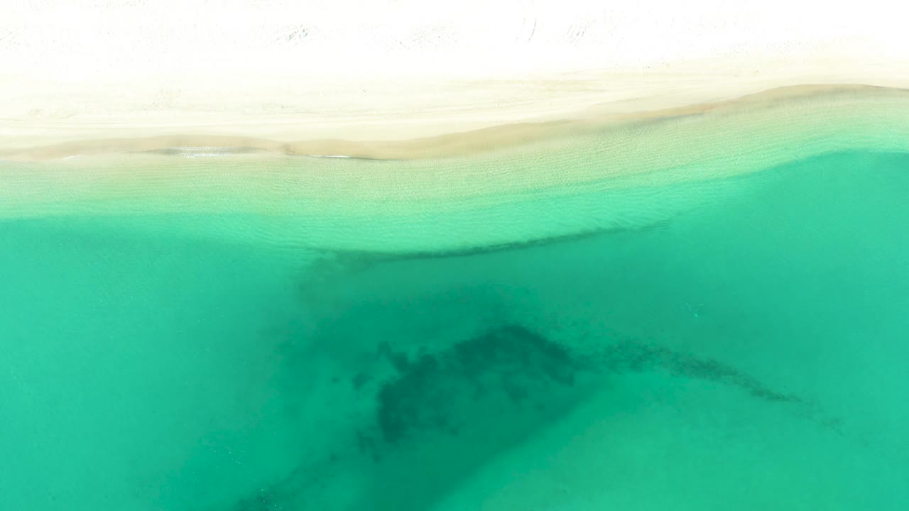 Top-down La Ribera shoreline view with pale sand across the top, translucent turquoise water below, and no visible people or structures.