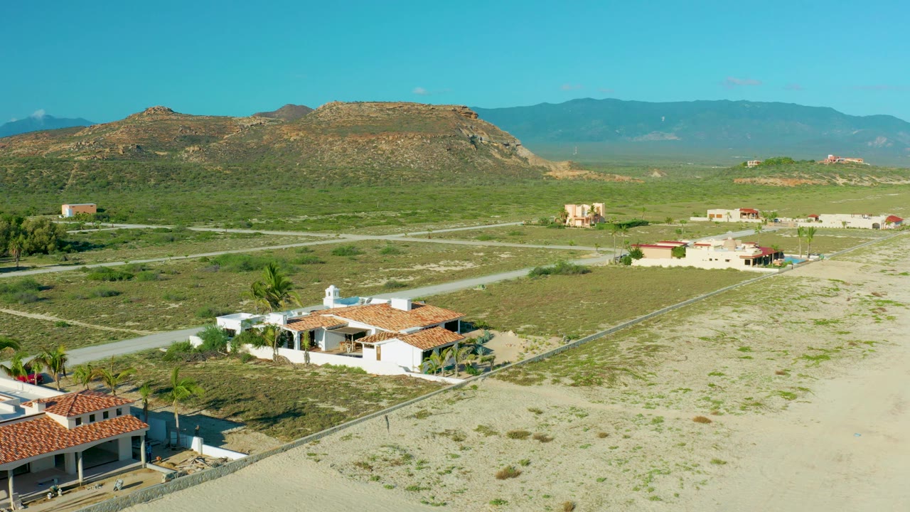 Aerial landscape with foreground homes, sandy ground, roads, scrub, and mesa.