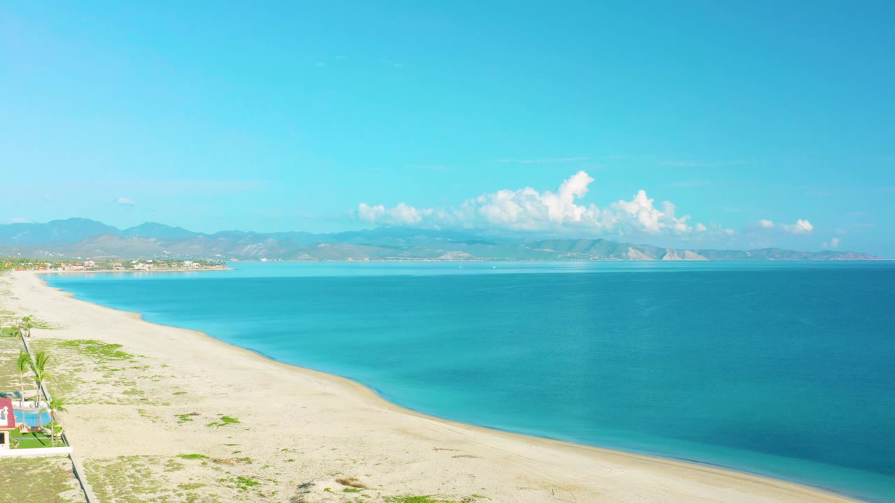 Second frame over La Ribera shows the beach curving farther into the distance, bright blue water filling the right side, and no visible people on the sand.