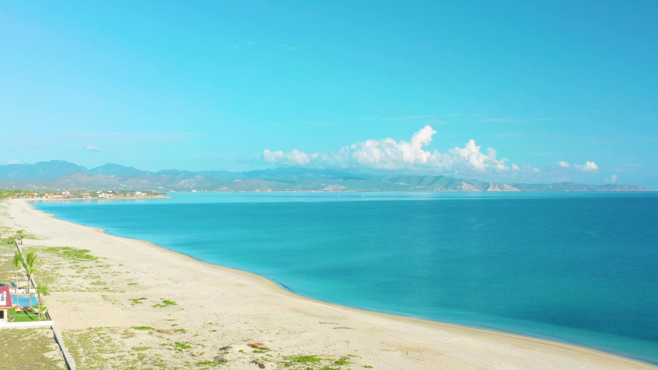 At 0:02, the La Ribera beach and water remain in a wide elevated composition, with the shoreline running diagonally and no visible people in frame.