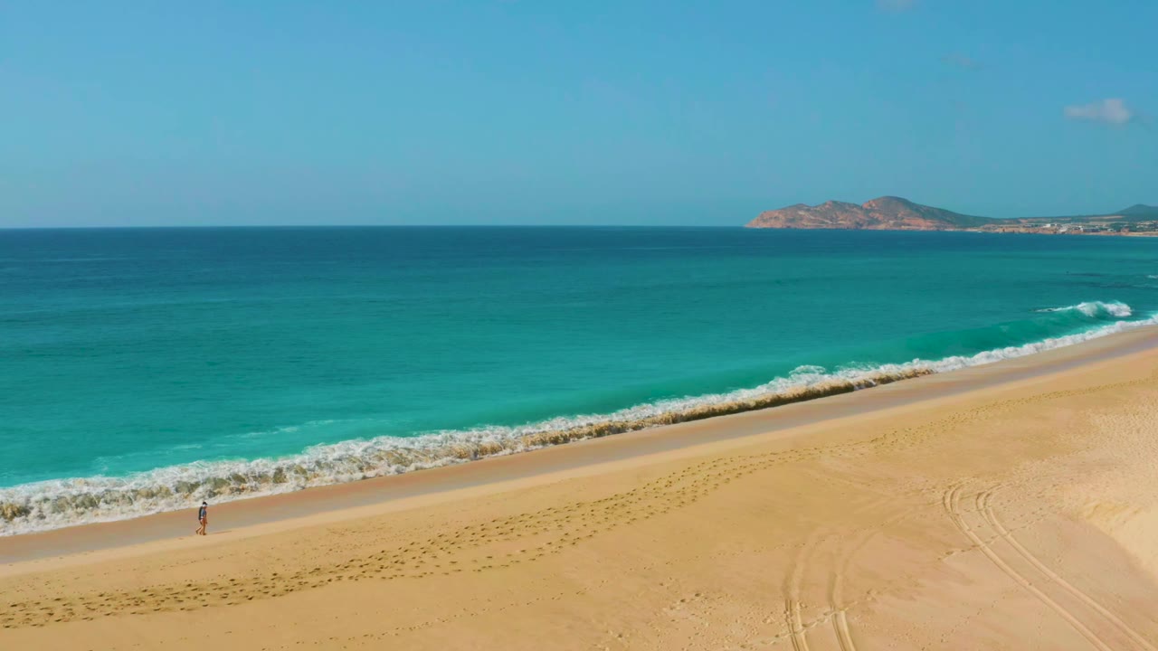 Two men walk along a wide sandy shoreline beside turquoise water.