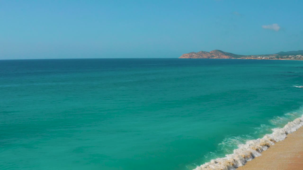 Open water dominates this Dreams Beach, Baja California Sur frame, with a small white surf streak near the lower right, distant rocky land, and no visible people.