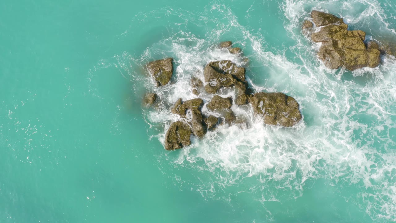Top-down view over Dreams Beach in Baja California Sur, Mexico, where white surf wraps the main rock group and a larger rock sits near the upper right edge, with no visible people.