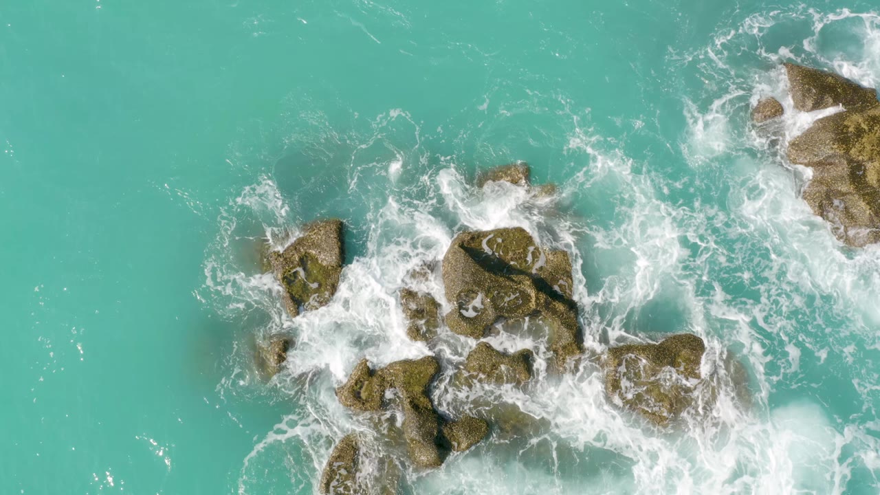 White surf spreads across the central rocks in blue-green water at Dreams Beach, Baja California Sur, Mexico, with open sea filling the frame and no visible people.