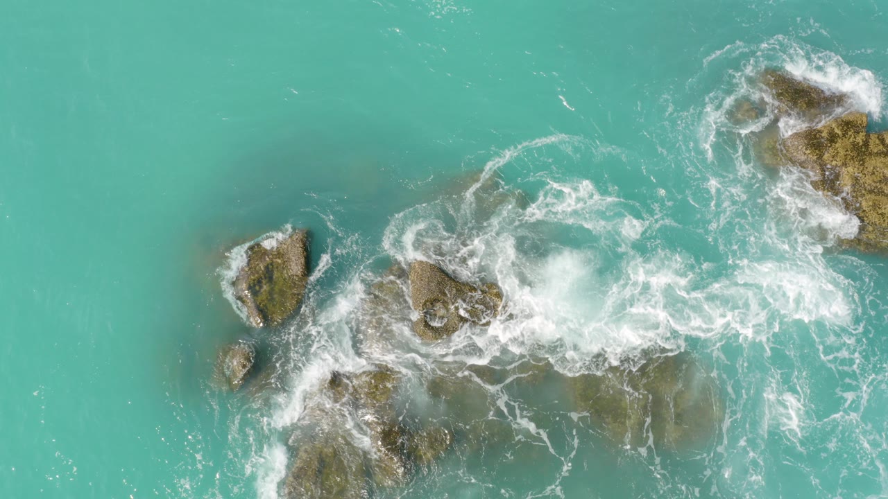Turquoise water and white surf around brown rocks