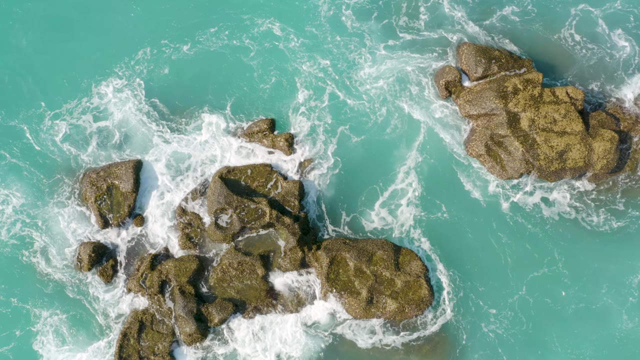 At Dreams Beach, Baja California Sur, white foam spreads across the central rock group while turquoise water remains open between the rocks, no visible people.