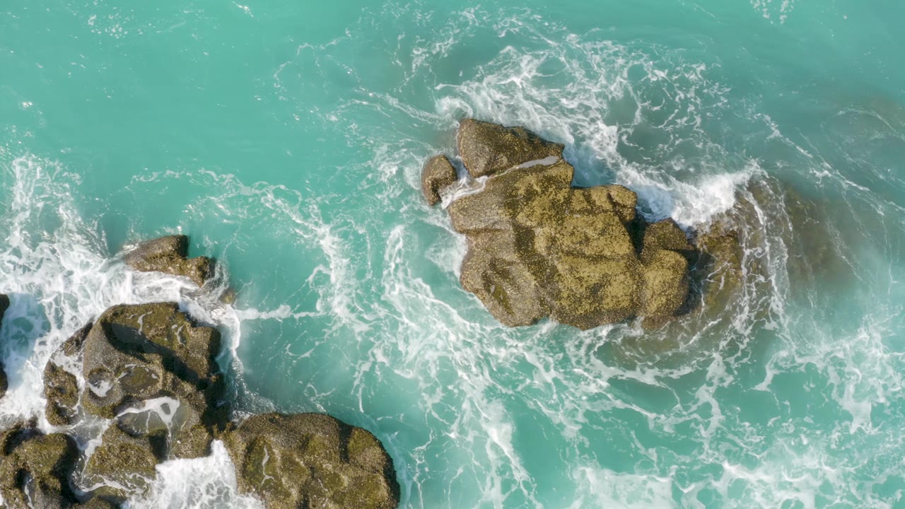 Large rock surrounded by swirling white foam and blue-green water