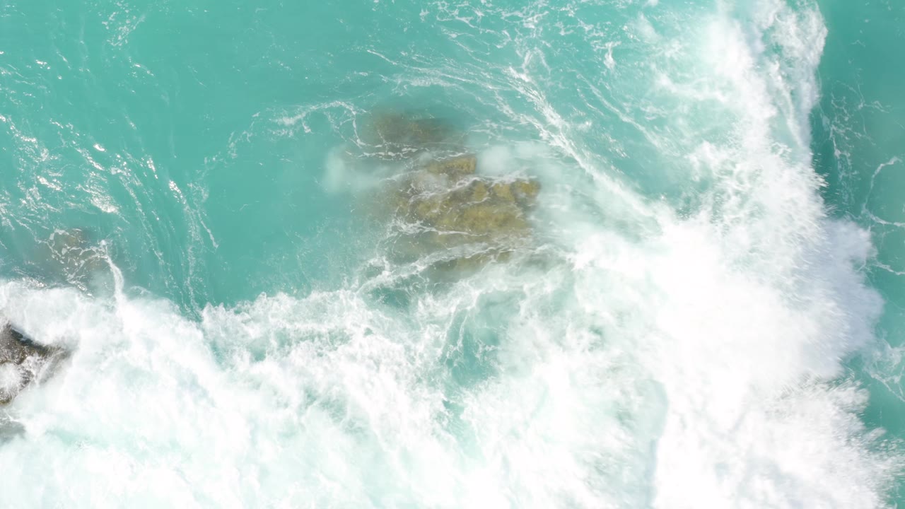 Dense white surf washes over partly submerged rocks, leaving only muted tan shapes visible beneath the foam at Dreams Beach, Baja California Sur, with no visible people.