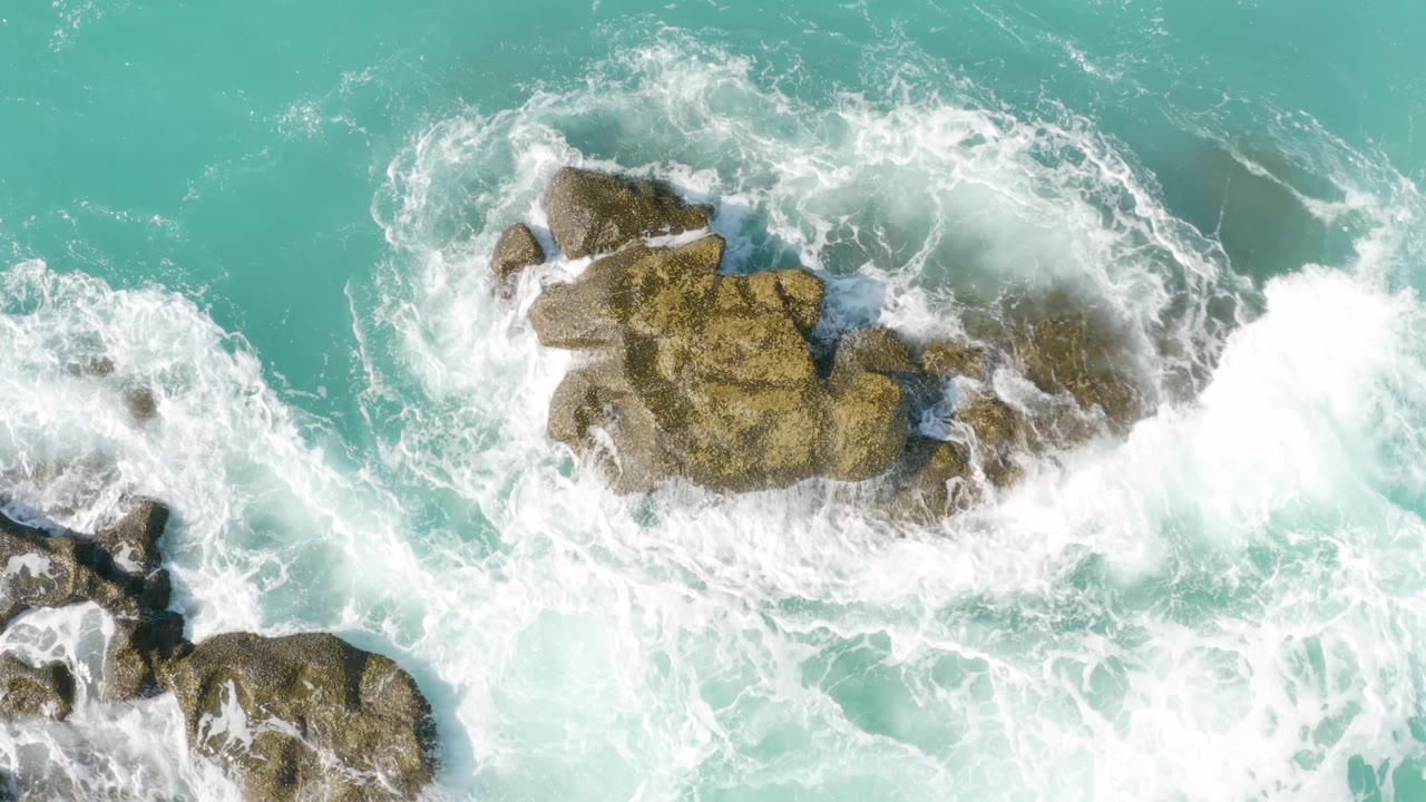 At 0:01, the drone-style overhead frame shows whitewater curling around a central rock cluster at Dreams Beach with no visible people.
