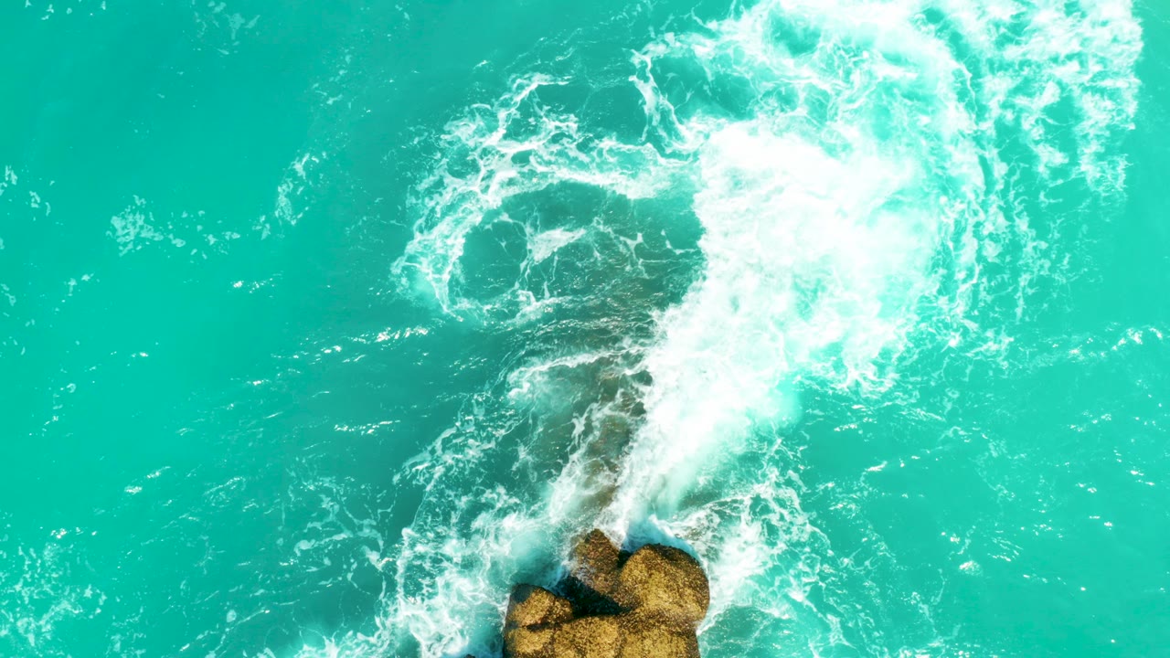 At 0:00, white surf spreads across turquoise water above tan rocks at Dreams Beach, Baja California Sur, Mexico, with no visible people.