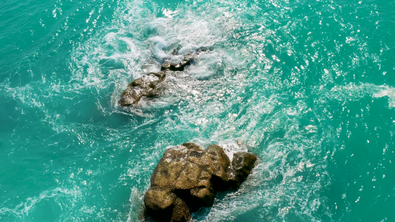 Turquoise water washing around two exposed rocks