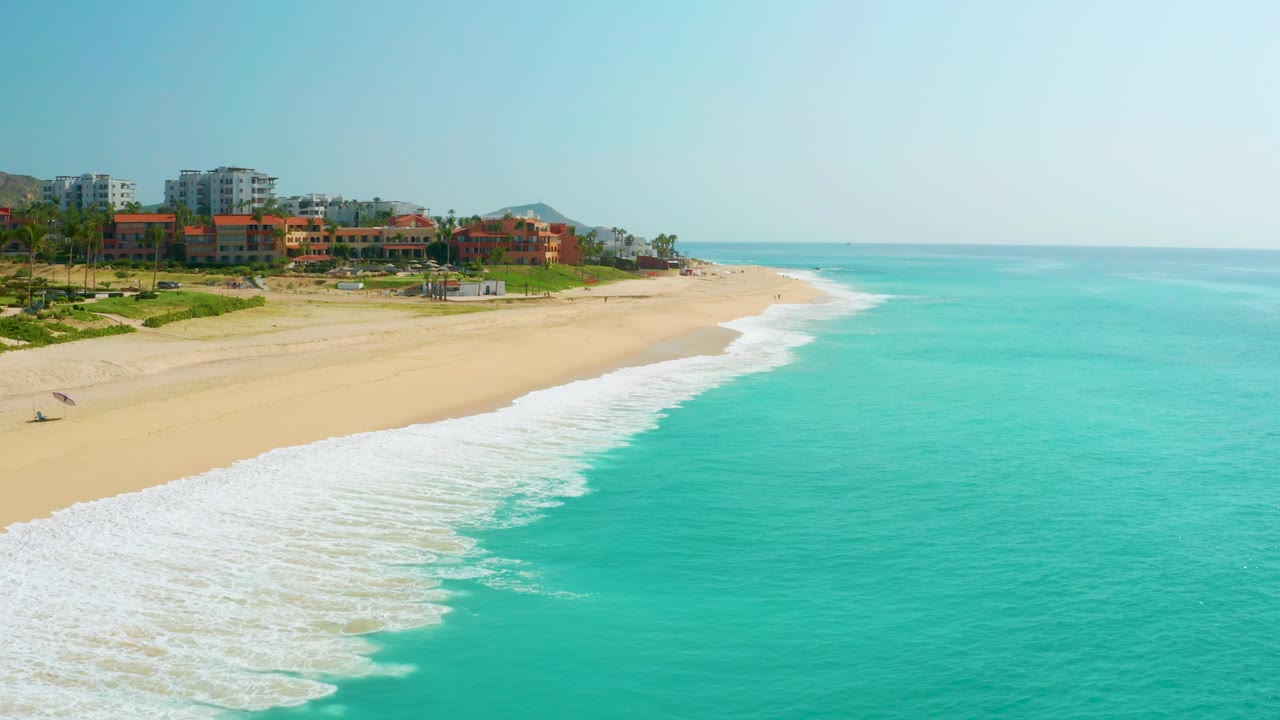 Foamy surf washes along the foreground with resort buildings beyond the beach.