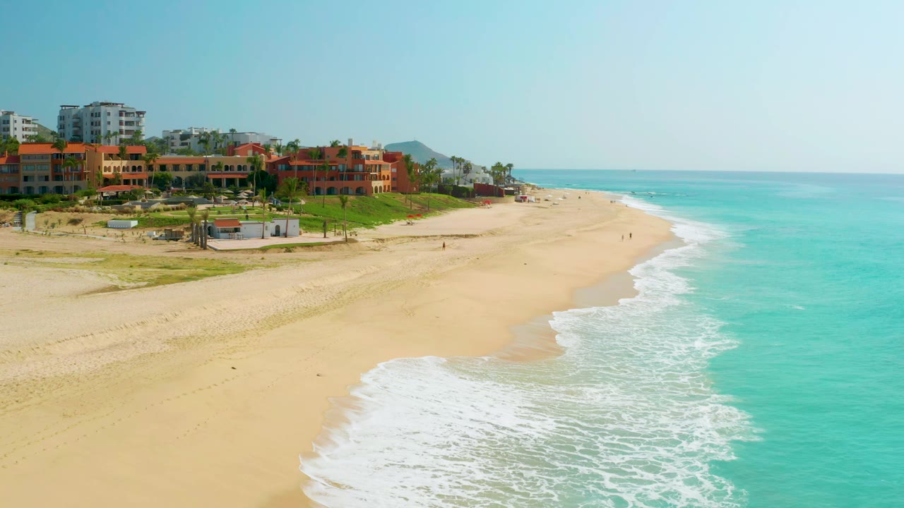 Aerial coastline view with foamy waves curving onto an open beach.