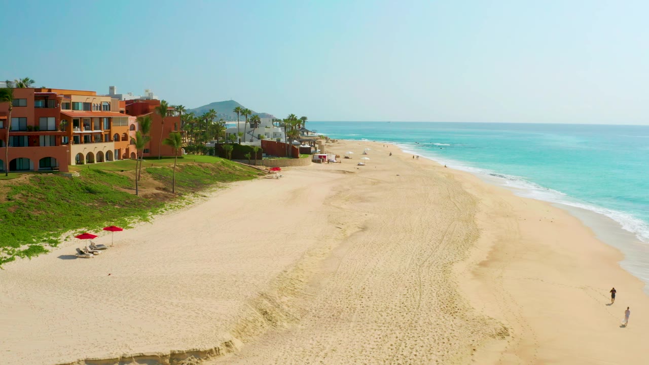 Aerial view of open sand, surf, palms, and beach buildings.