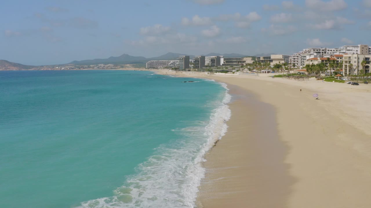 High coastal view of turquoise sea, sandy shore, palms, and modern beachfront buildings.