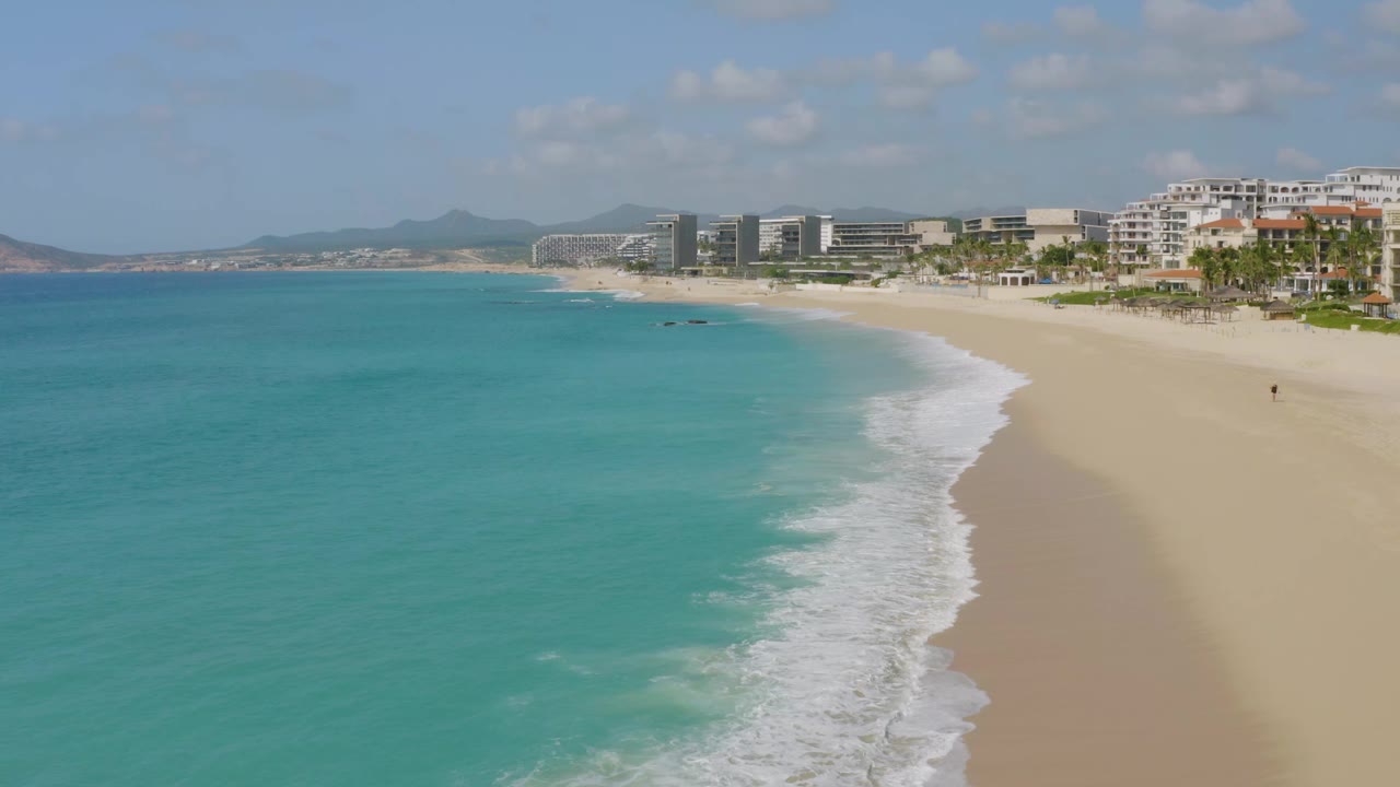 Aerial shoreline view with waves curling diagonally along a broad empty beach.