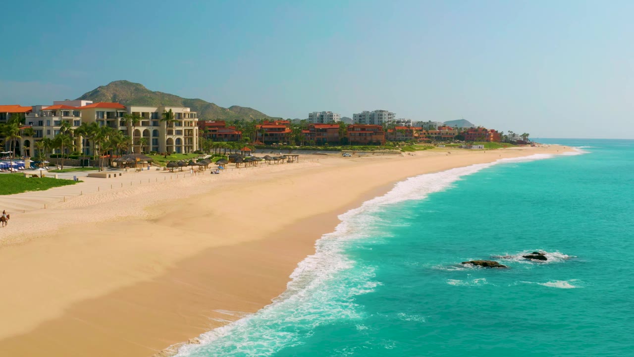 At 0:01, the Dreams Beach aerial angle holds the shoreline across the frame, with white surf separating golden sand from turquoise water and no visible people.
