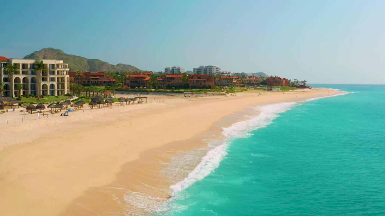 Aerial view of the Baja California Sur resort beach with more open water filling the right side, a broad sand curve in the center, and no visible people.