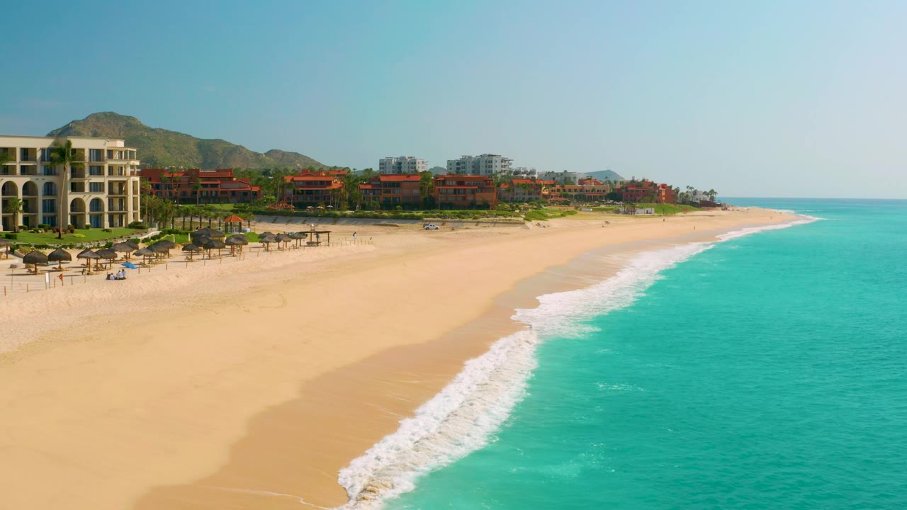Beach resort shoreline seen from above with surf rolling onto sand.