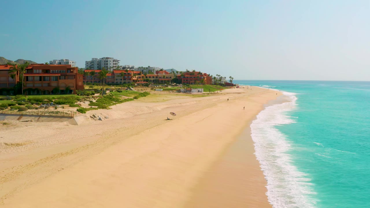 Dreams Beach aerial frame with the surf line curving closer to the center and beachfront buildings continuing along the left background.