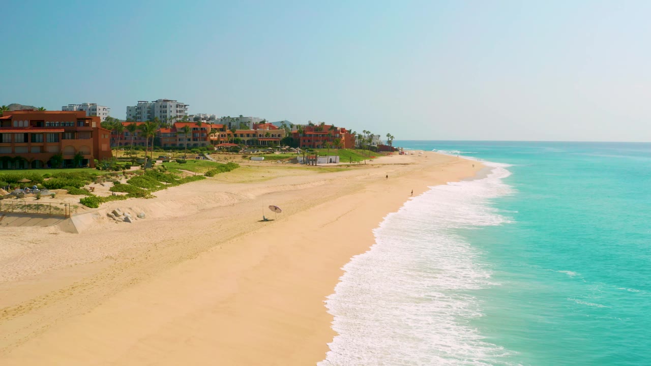 Aerial coastline view with resort buildings at left and surf sweeping across the beach.