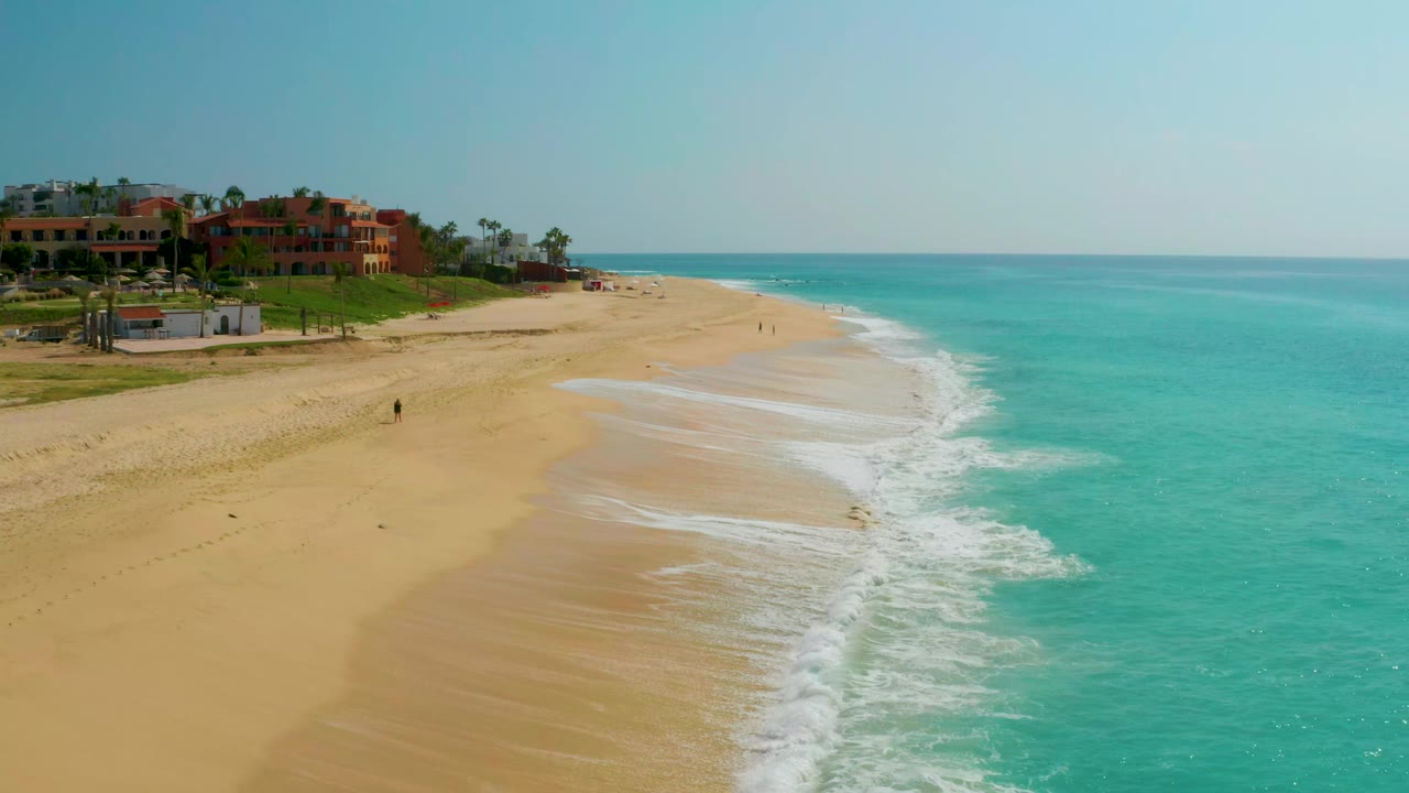 Elevated shoreline view with surf curling beside a wide sandy beach.
