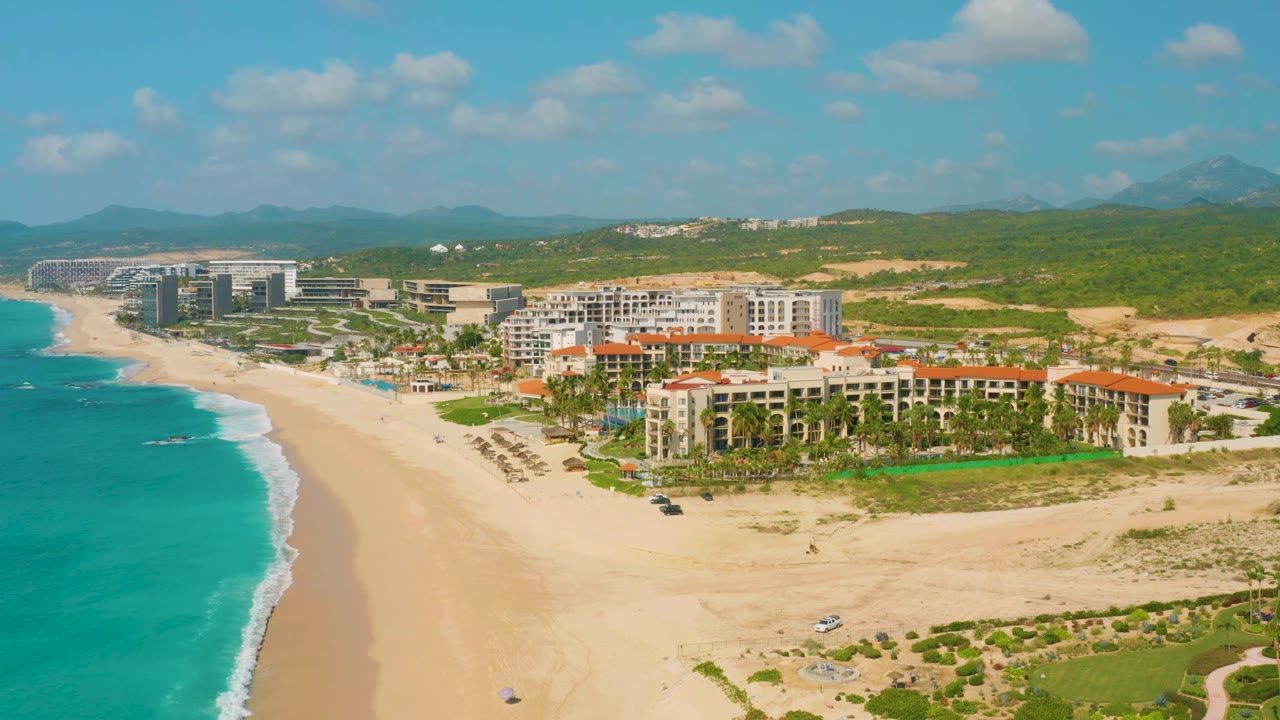 Wide aerial of resort hotels beside a long sandy beach and blue shoreline.
