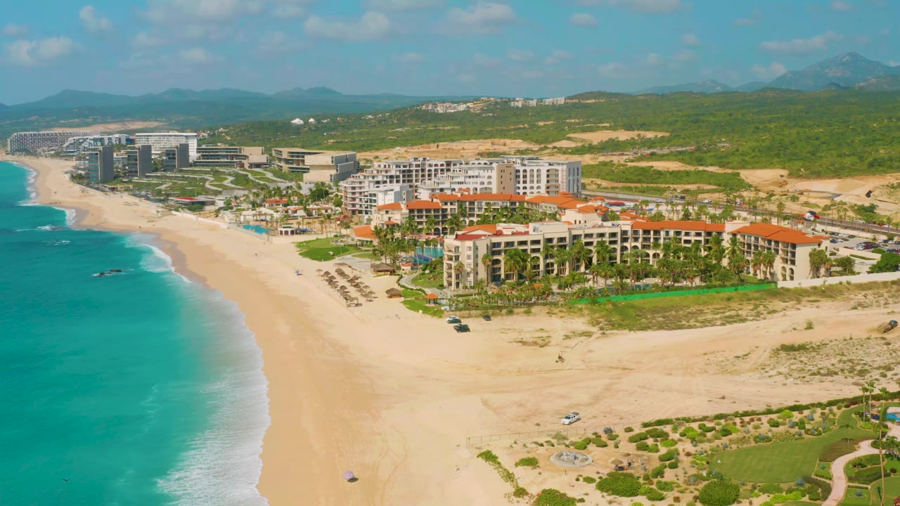 Second frame keeps the Dreams Beach shoreline at left with white surf edging the sand, while the resort complex sits closer to center under a clear blue sky and no visible people appear.